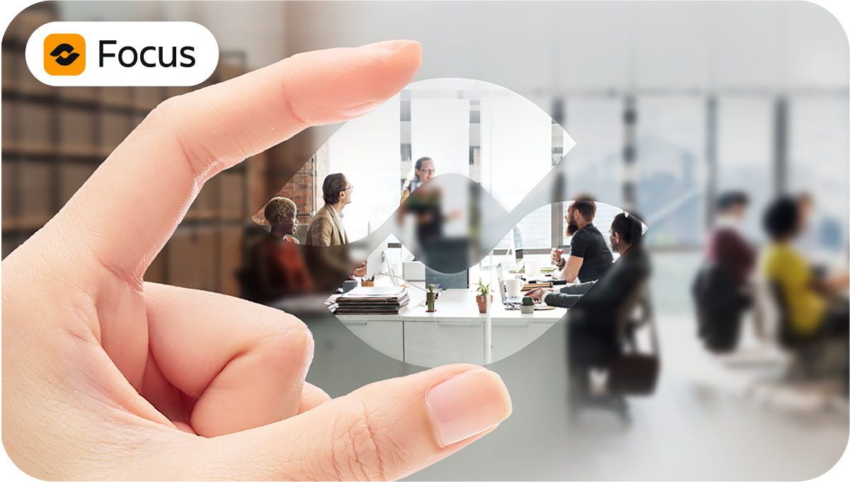 Atlassian Focus - Das strategische Portfolio-Management für Ihr Unternehmen 11 Atlassian Focus Schaubild: Im Hintergrund ist eine unscharfe Szene eines Teams im Meeting, im Vordergrund hält eine Hand das Atlassian Focus Logo wie eine Linse durch die das Team scharf und klar zu sehen ist.